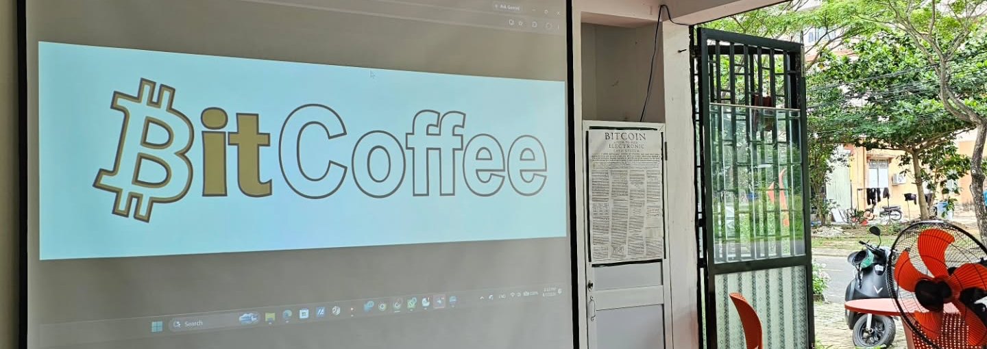 Đêm chiếu phim tại BitCoffee, Sơn Trà, Đà Nẵng - logo ₿itCoffee chiếu trên màn hình máy chiếu, laptop hiển thị logo ₿itCoffee trên bàn, ghế cà phê màu cam